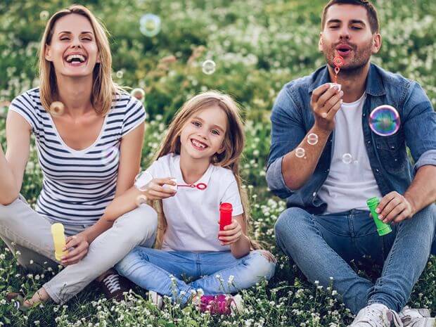 A family blowing bubbles whilst sitting on the grass outside.