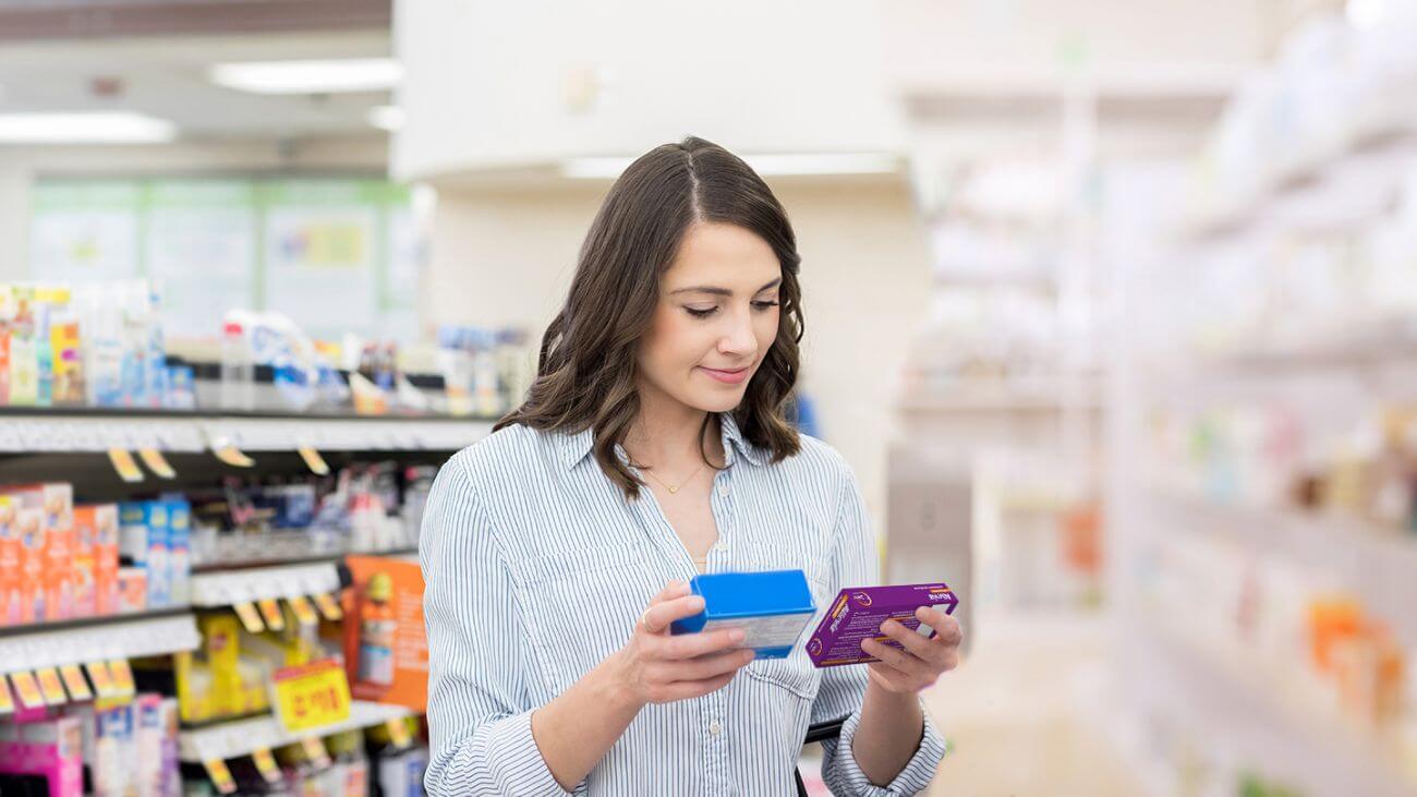 A woman comparing Allevia® with another medicine in the allergy aisle at a store, looking approvingly towards Allevia®.