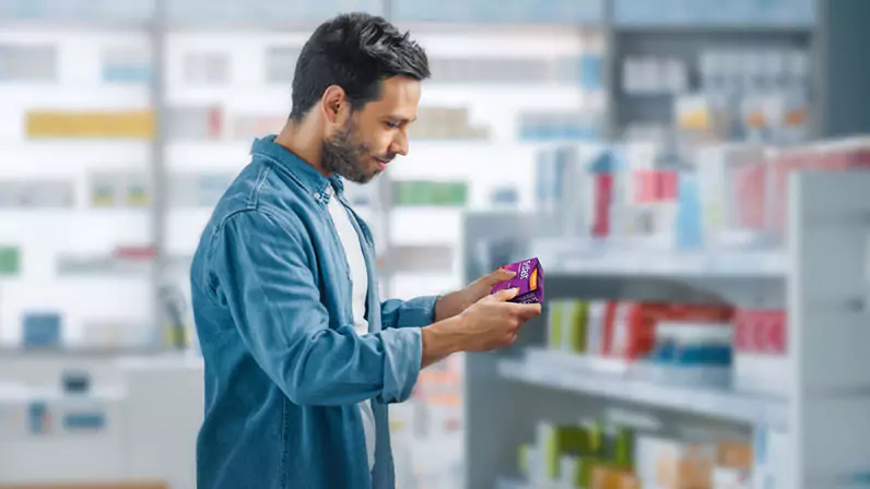 A man in the pharmacy aisle reading the back of the Allevia Allergy pack.